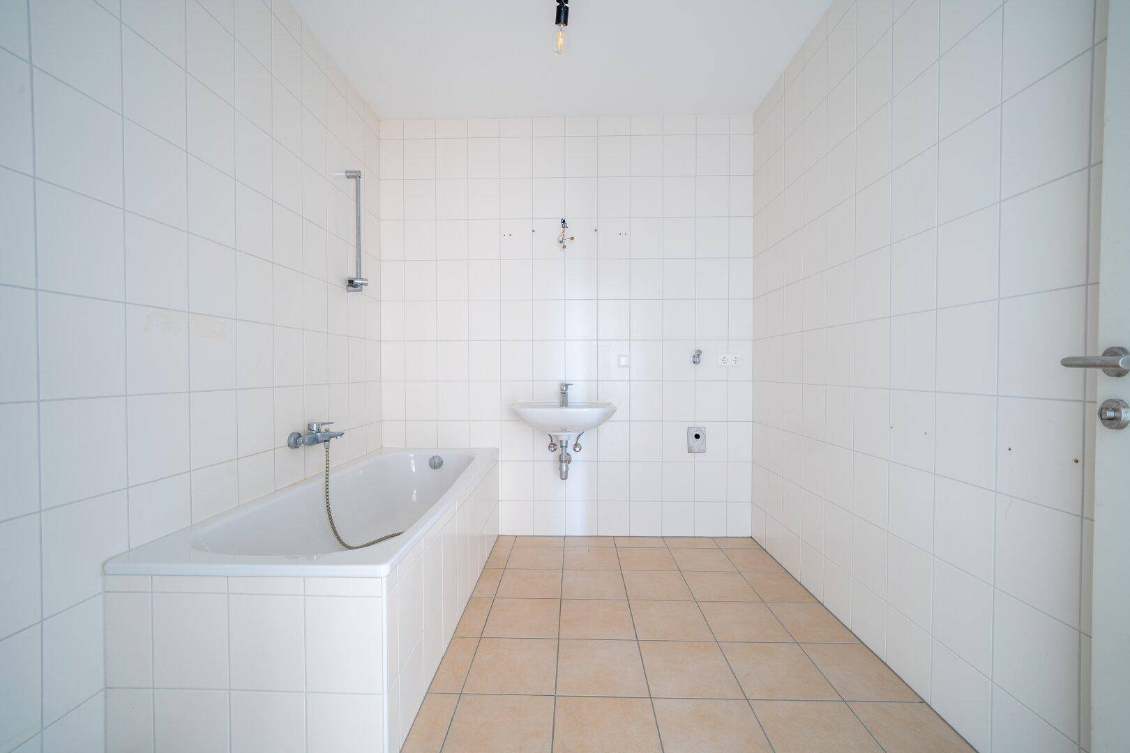 Geräumiges Badezimmer mit Badewanne, Waschbecken und Anschluss für eine Waschmaschine, komplett gefliest.
