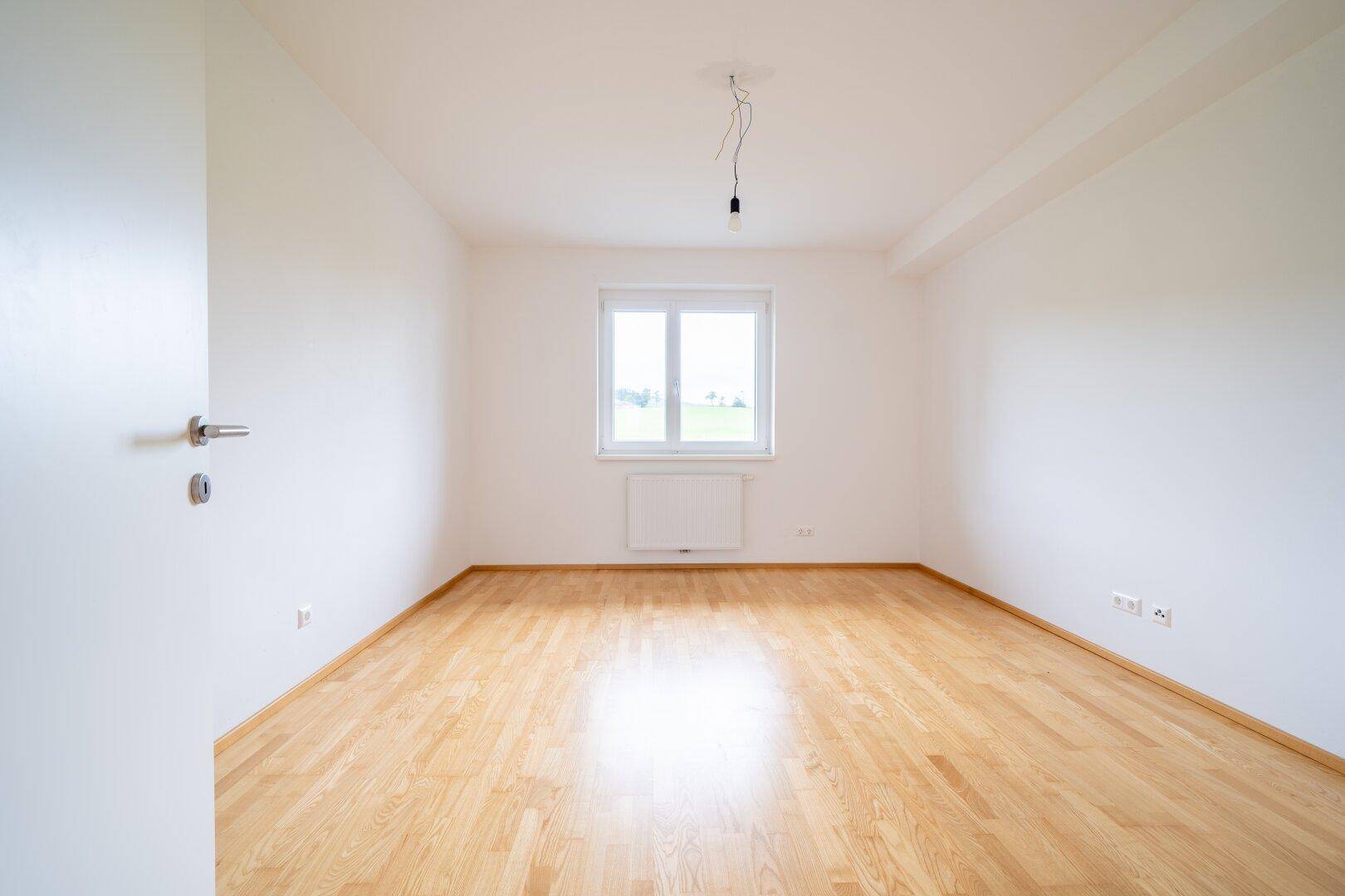 Geräumiges Schlafzimmer mit Parkettboden und großem Fenster, das viel natürliches Licht spendet.