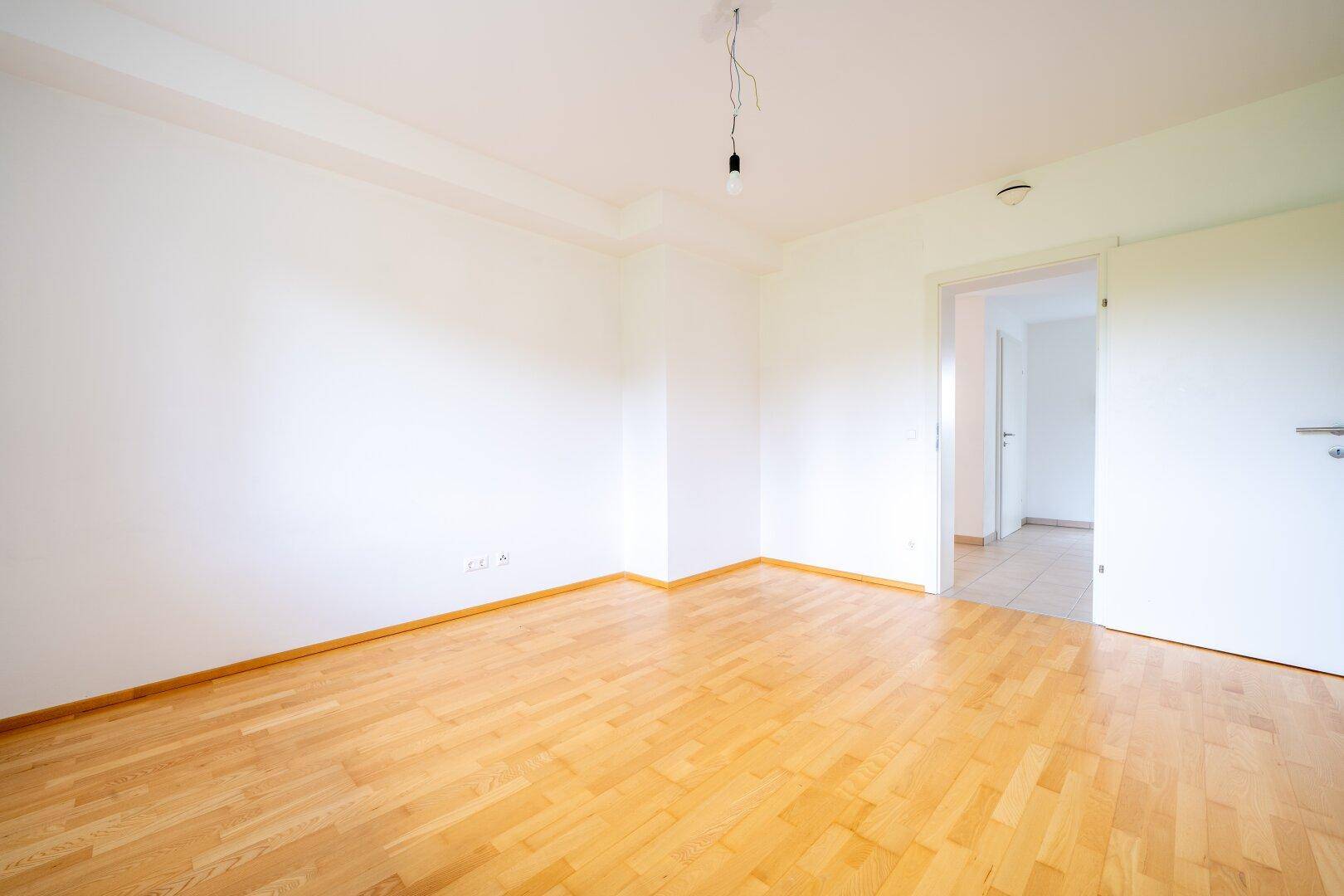 Schlafzimmer mit Parkettboden und weiß gestrichenen Wänden, bietet Zugang zu einem angrenzenden Bereich.
