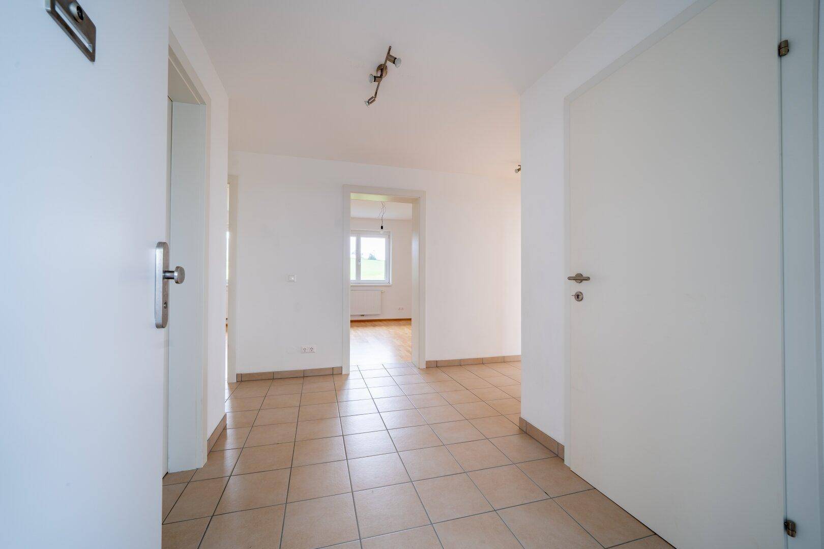 Heller Flur mit Fliesenboden, der zu den Zimmern mit Parkett führt und eine offene Atmosphäre schafft.