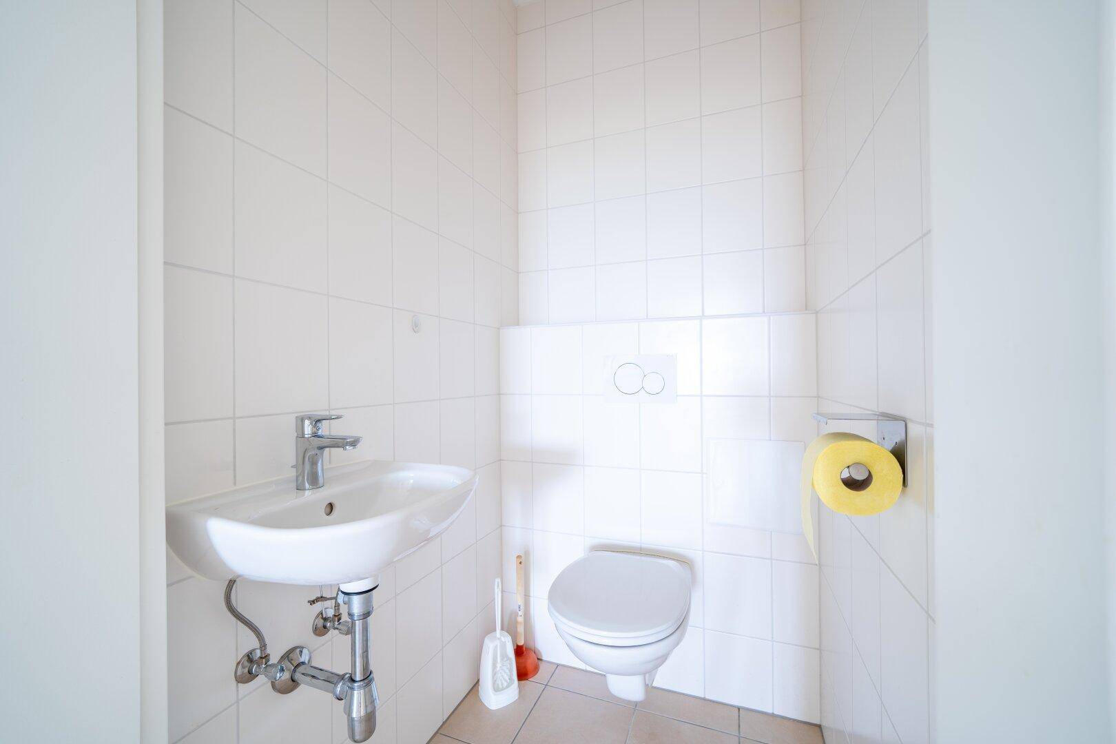 Separates Gäste-WC mit weißen Fliesen, Toilette und kleinem Handwaschbecken, praktisch und funktional.