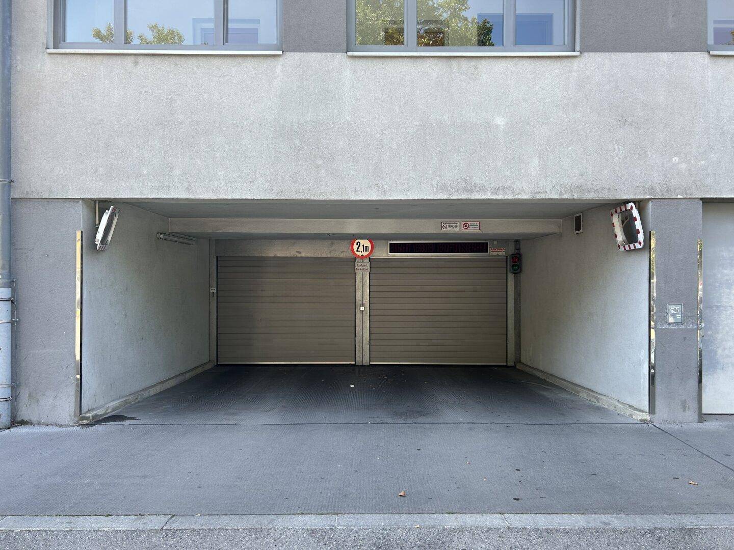 Eingang zu einer Tiefgarage mit zwei Rolltoren unter einem modernen Wohngebäude.
