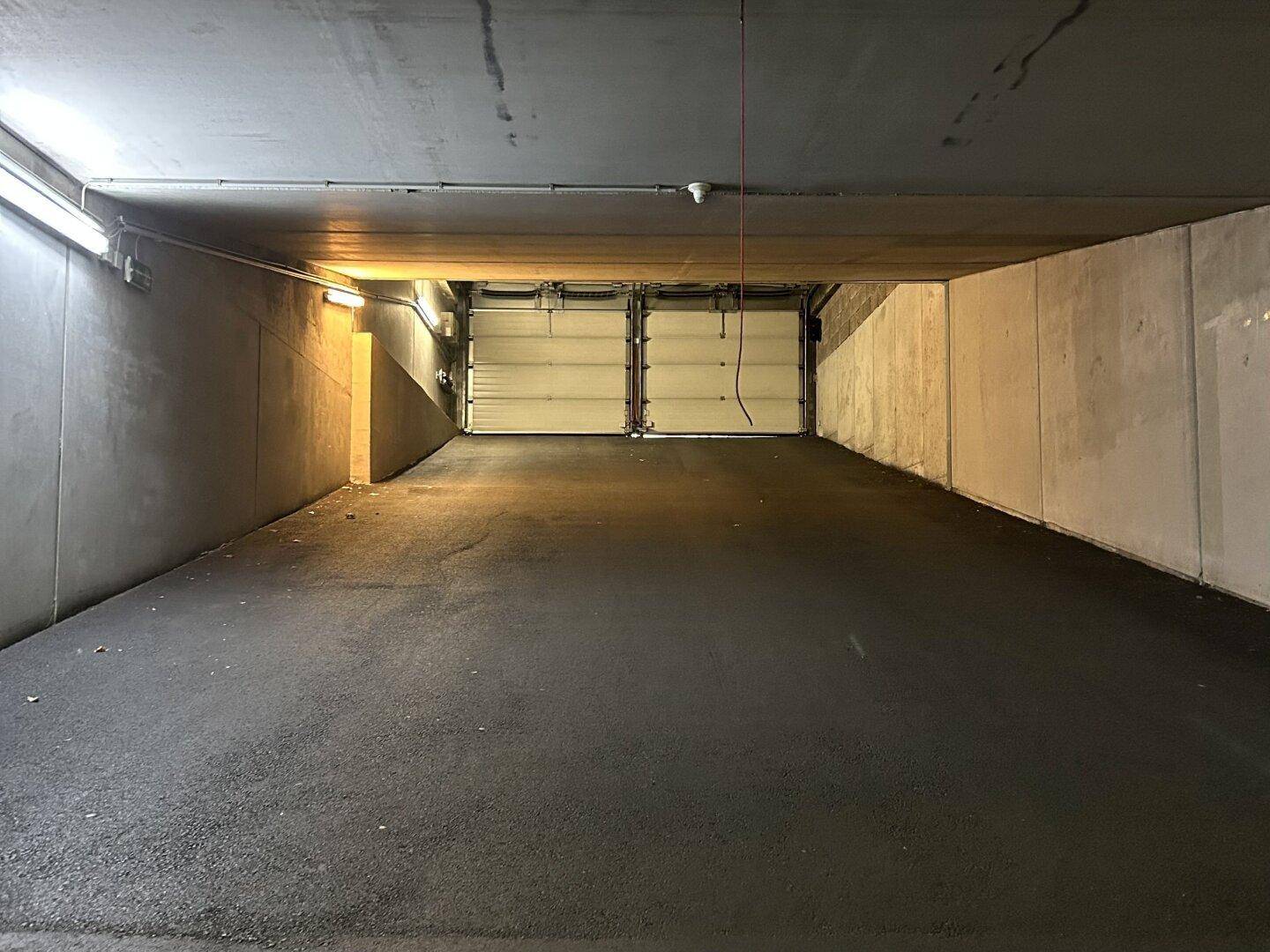 Geräumiger leerer Bereich einer Tiefgarage, der zu zwei geschlossenen Garagentoren führt.
