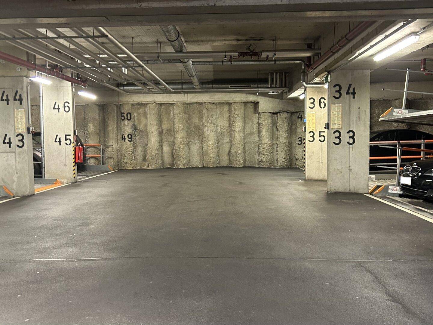 Leerer Parkbereich in einer Tiefgarage mit Betonwänden, Säulen und sichtbaren Deckeninstallationen.