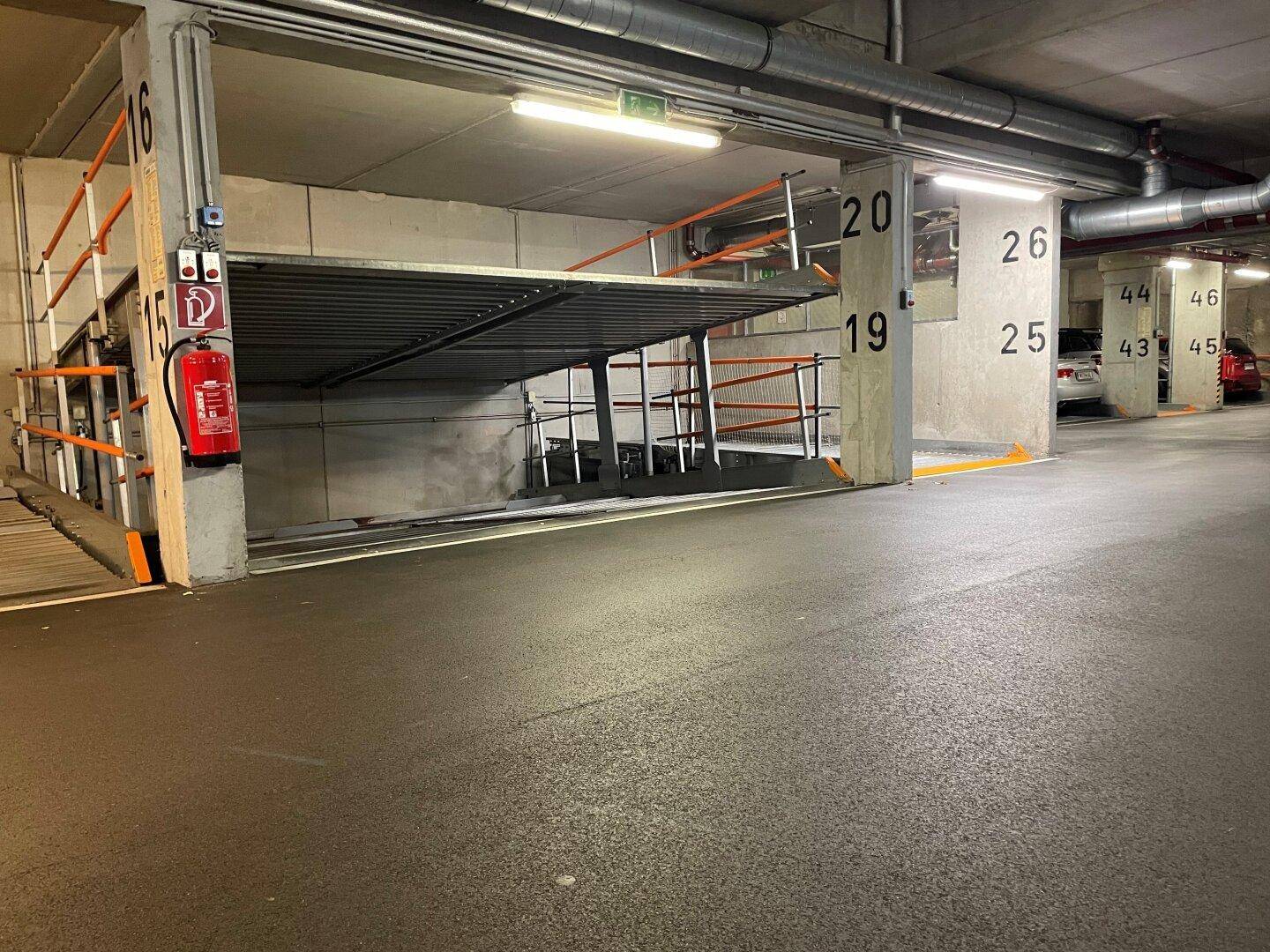 Moderne Tiefgarage mit Doppelparker-System, nummerierten Stellplätzen und sichtbaren Installationen an der Decke.
