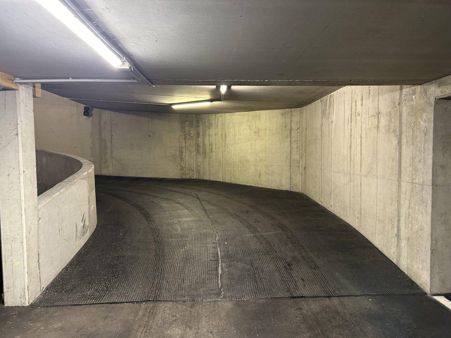 Geschwungene Zufahrtsrampe zur Tiefgarage mit robusten Betonwänden und rutschfestem Bodenbelag.