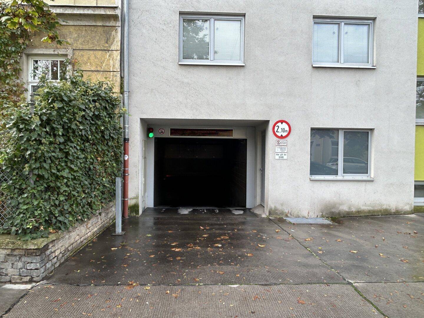 Einfahrt zur Tiefgarage mit Höhenbegrenzung, umgeben von einer Gebäudefassade und Grünflächen.