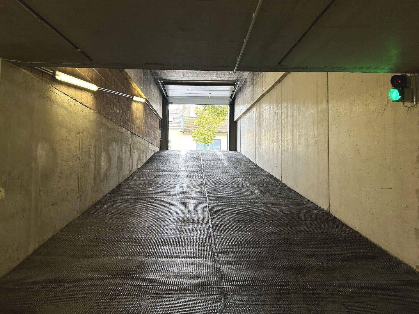 Ausfahrt einer Tiefgarage mit strukturierter Rampe und Blick ins Freie mit Tageslicht.
