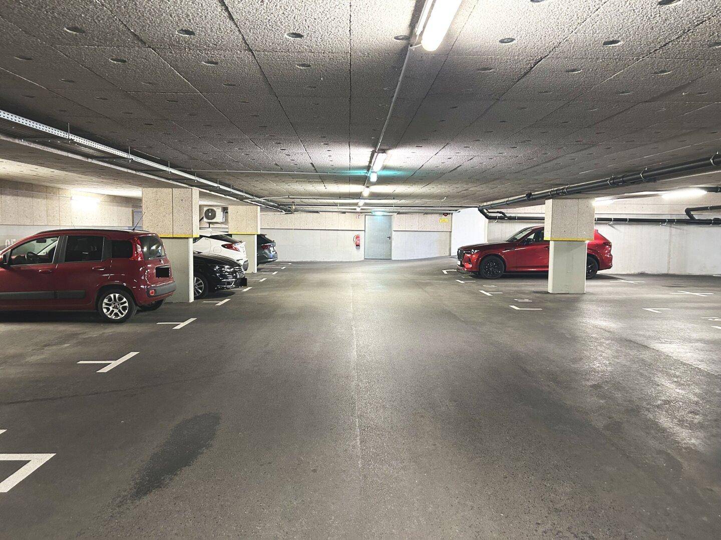 Helle Tiefgarage mit markierten Stellplätzen und geparkten Fahrzeugen, gut beleuchtet.