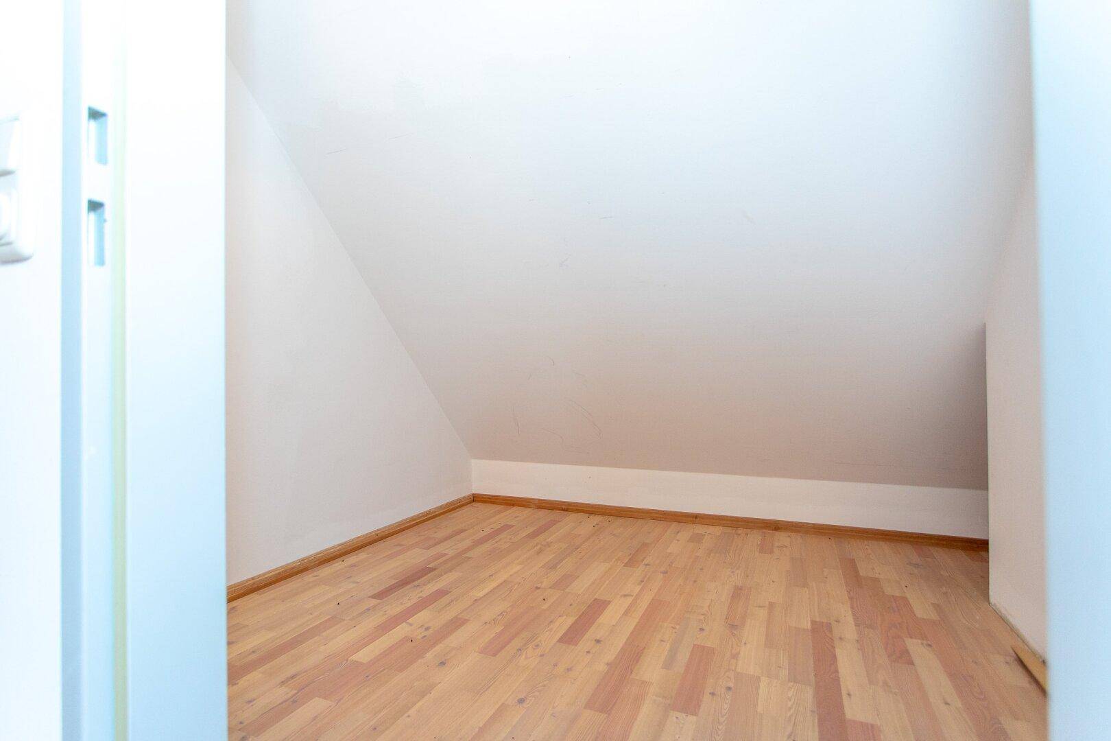 Kleiner, heller Raum mit Parkettboden und Dachschräge, ideal als Abstellraum oder kleines Arbeitszimmer.