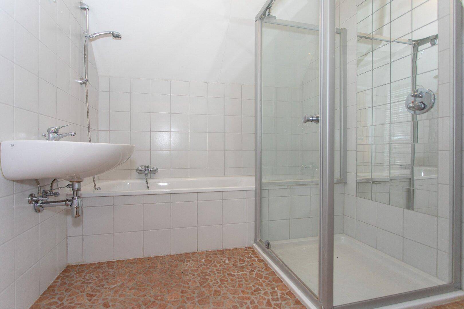 Badezimmer mit Badewanne, Duschkabine und Waschbecken, ausgestattet mit weißen Fliesen und Mosaikboden.