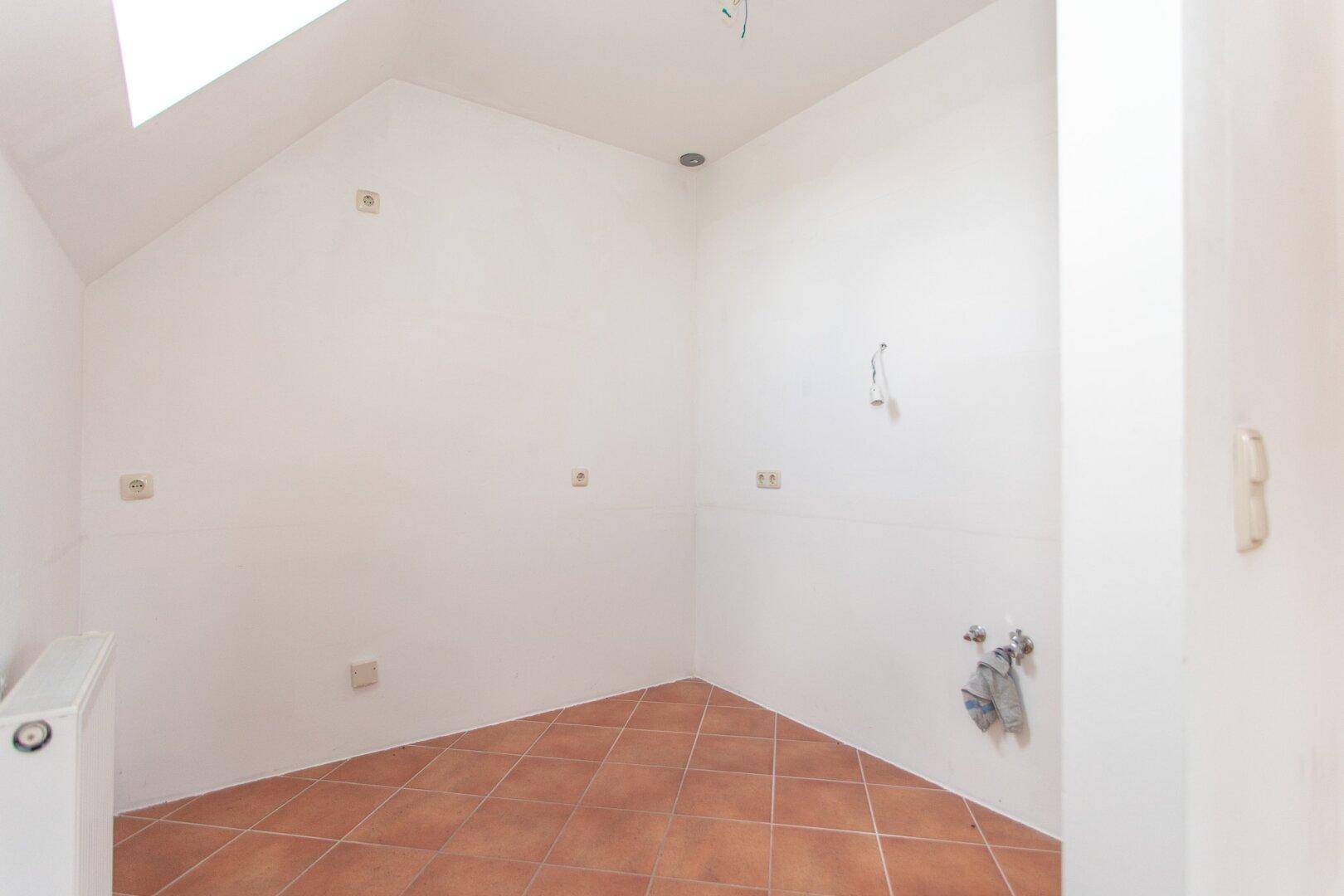Leerer Raum mit Terracotta-Fliesenboden, Dachschräge und Anschlüssen für eine zukünftige Küche.
