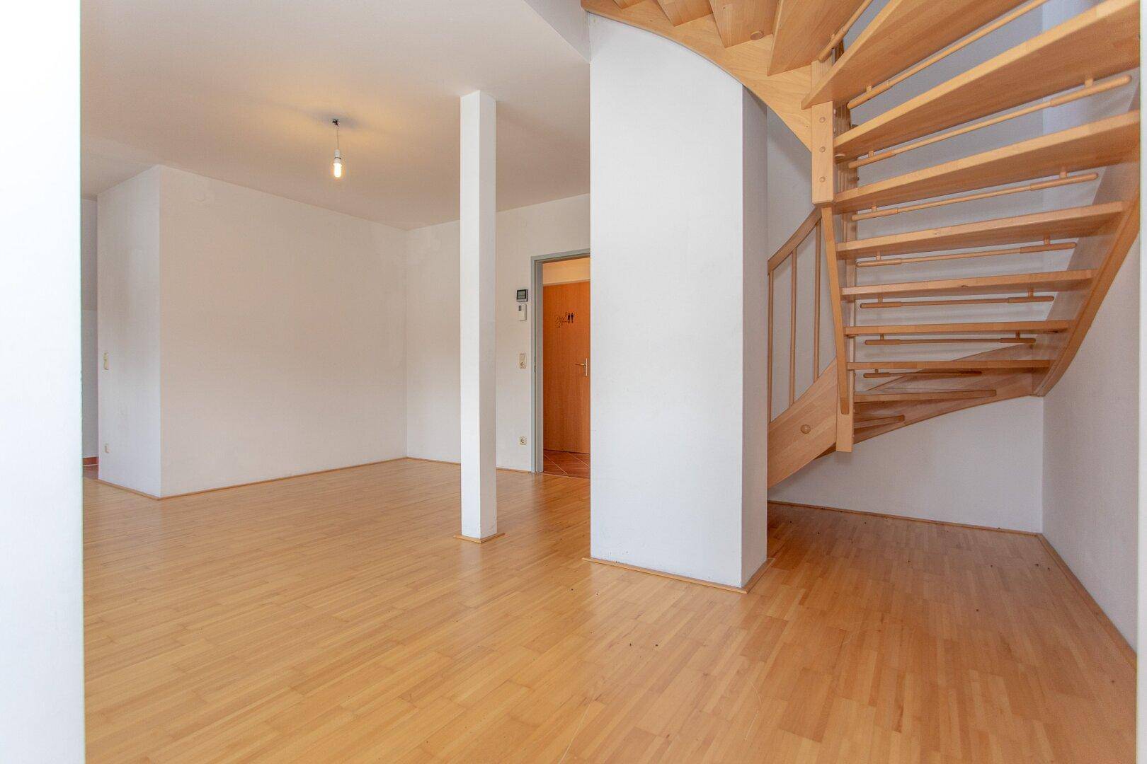 Geräumiger Wohnbereich mit Parkettboden und einer eleganten Holztreppe, die den oberen Bereich erschließt.
