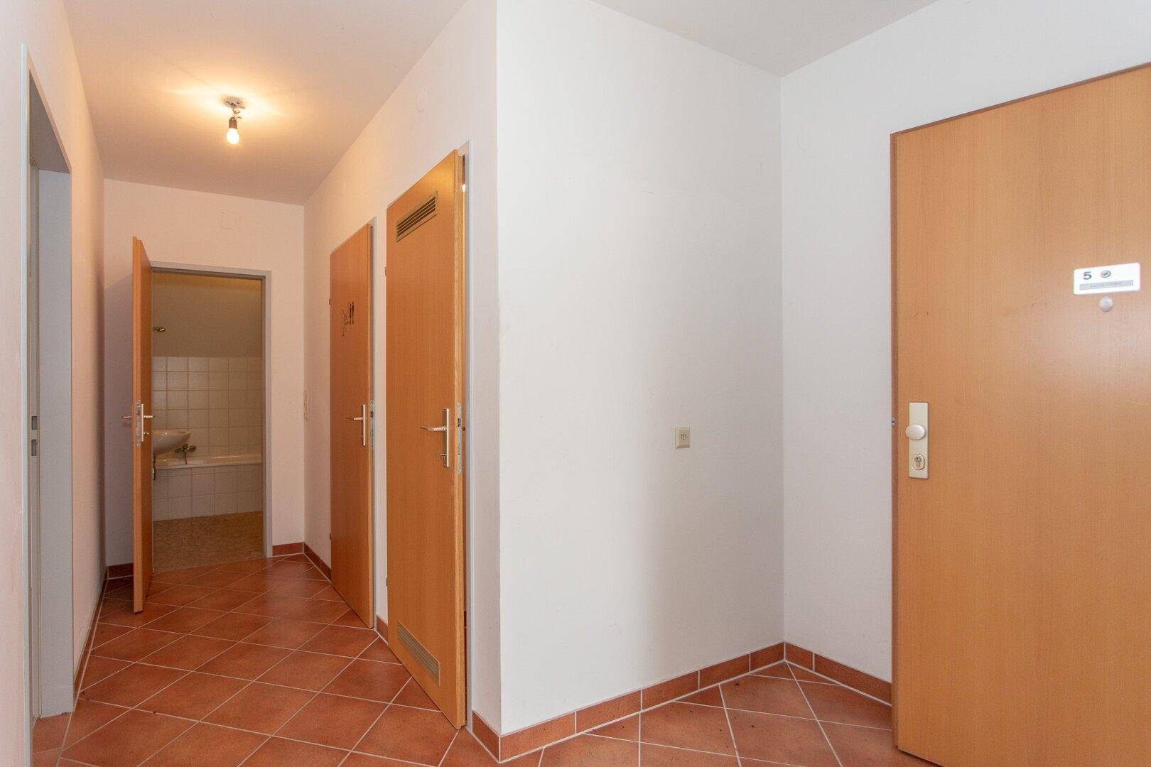 Eingangsbereich mit Terracotta-Fliesenboden und mehreren Holztüren, die zu verschiedenen Zimmern führen.