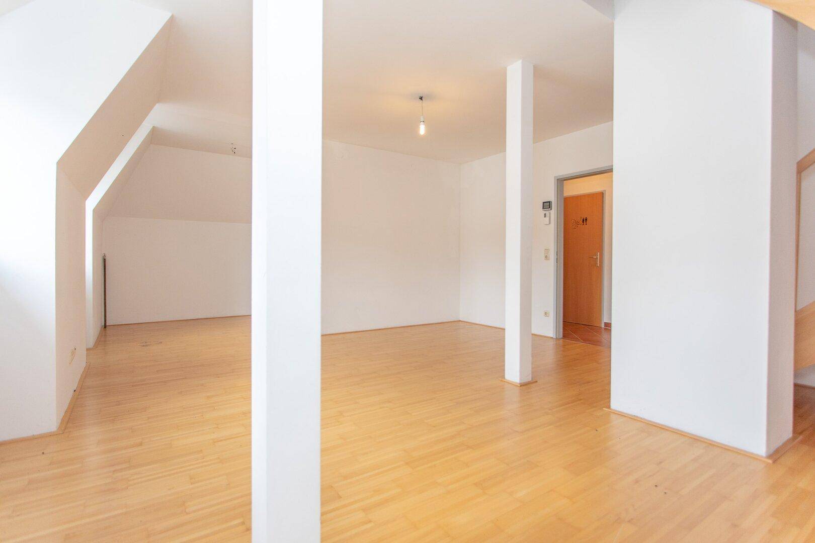 Geräumiger, heller Wohnbereich mit Parkettboden und einem Durchgang zu einem weiteren Zimmer oder Flur.