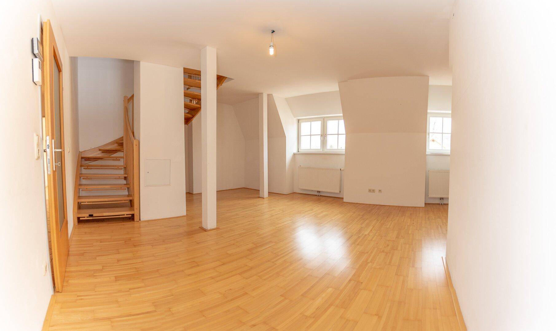 Offener Wohnbereich mit Parkettboden, Dachschrägen und einer eleganten Holztreppe, die den Raum strukturiert.