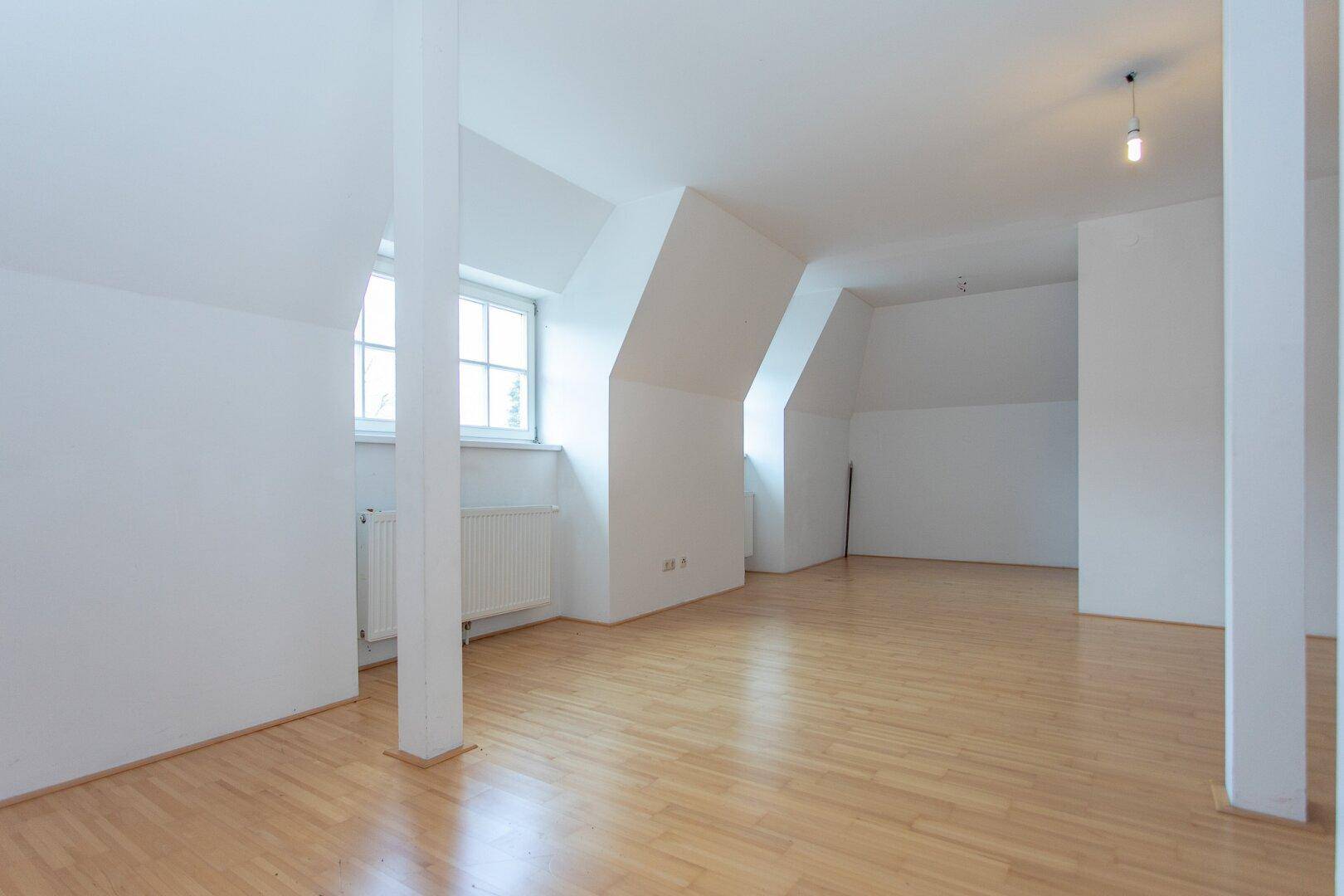Geräumiger Wohnbereich mit hellen Wänden, Parkettboden und Fenstern in den Dachschrägen, die viel Licht hereinlassen.