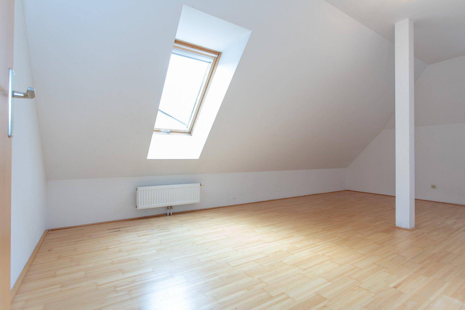 Helles Zimmer im Dachgeschoss mit Parkettboden, Dachschräge und einem großen Dachfenster für viel Tageslicht.