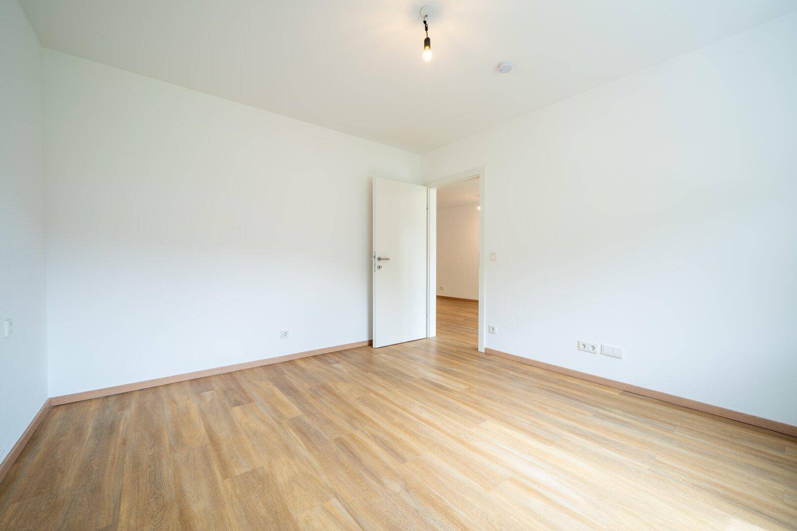 Leeres Zimmer mit Laminatboden und weiß gestrichenen Wänden, ideal als Schlaf- oder Arbeitszimmer.