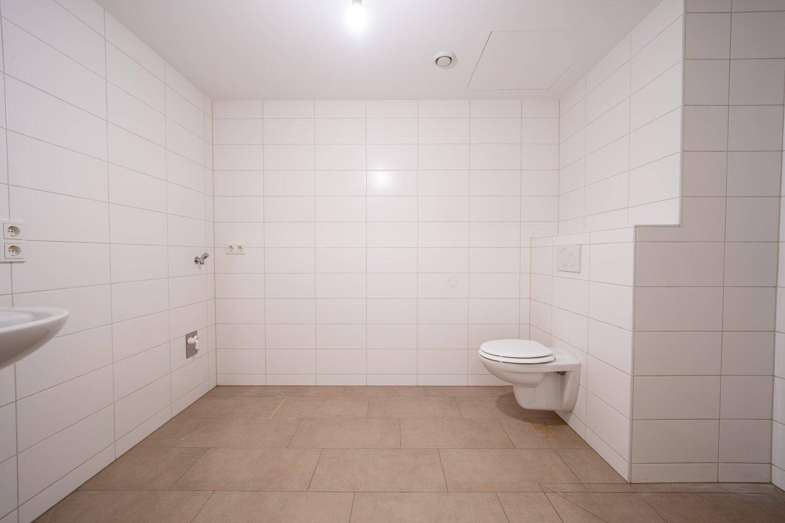 Modernes Badezimmer mit weißen Wandfliesen, beigem Boden und wandhängendem WC.