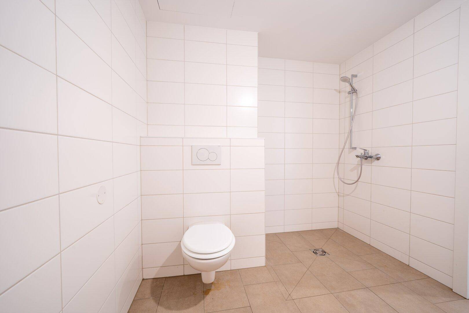 Funktionales Badezimmer mit weißen Fliesen, Duschbereich und wandhängendem WC.