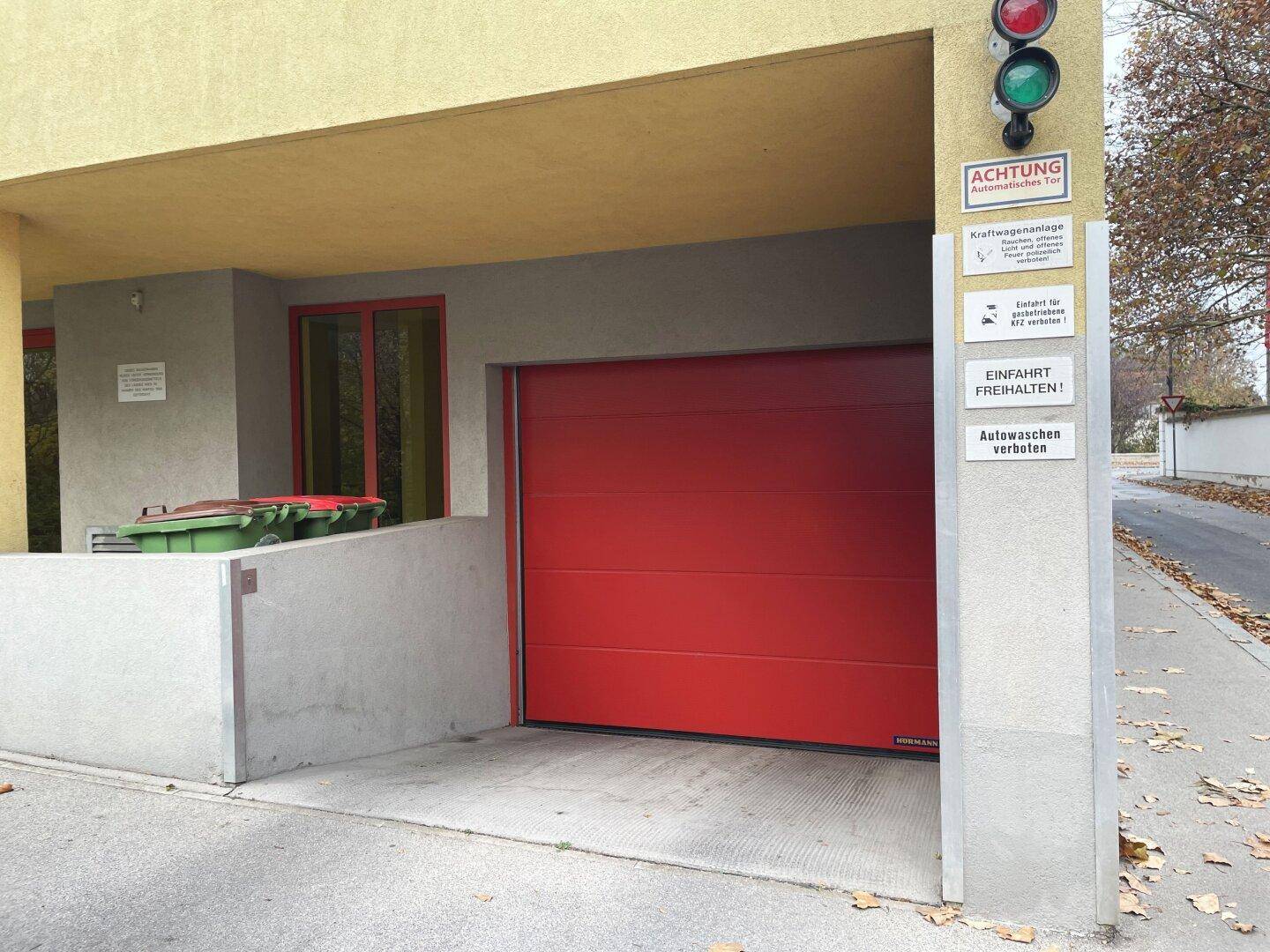 Rotes Garagentor mit Ampel und Hinweisschildern an der Einfahrt zu einer Tiefgarage.