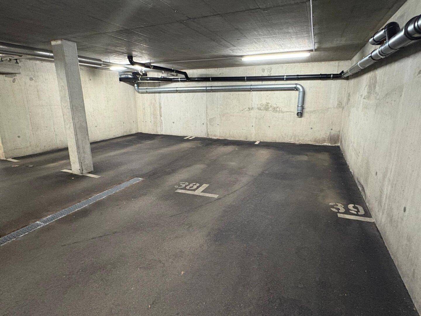 Tiefgaragenstellplätze mit Betonwänden, sichtbaren Rohren und Beleuchtung, bereit zur Nutzung.