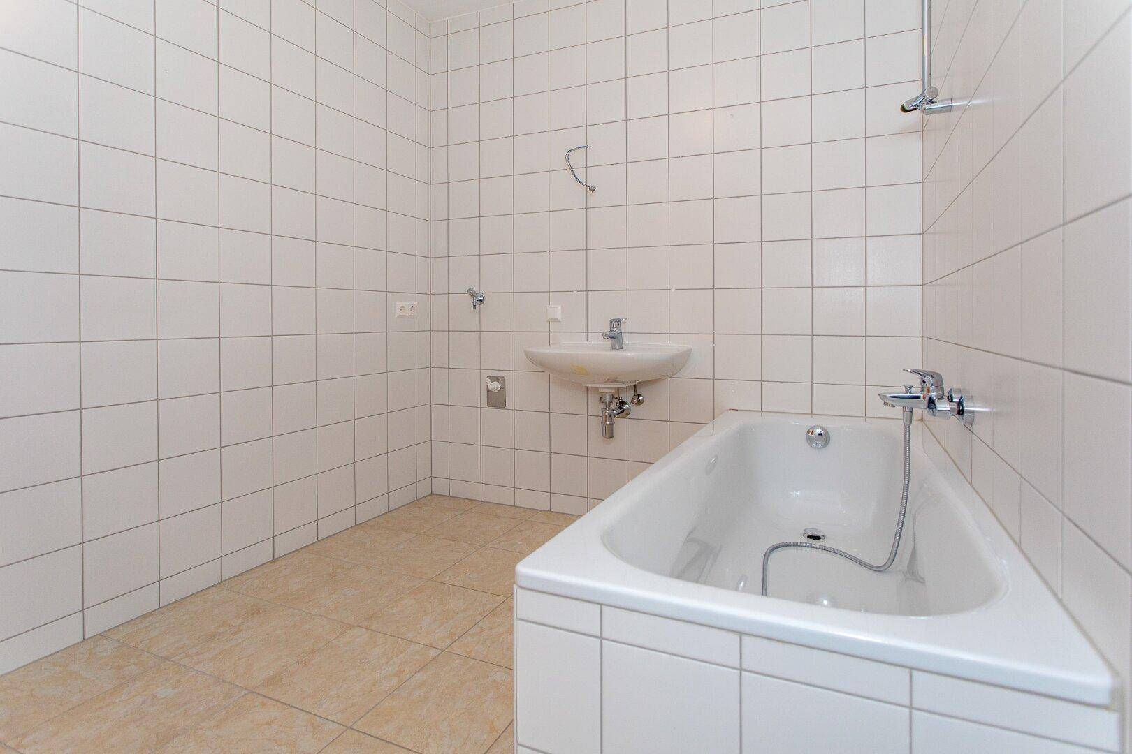 Modern gefliestes Badezimmer mit Badewanne und Waschbecken in heller Farbgebung.