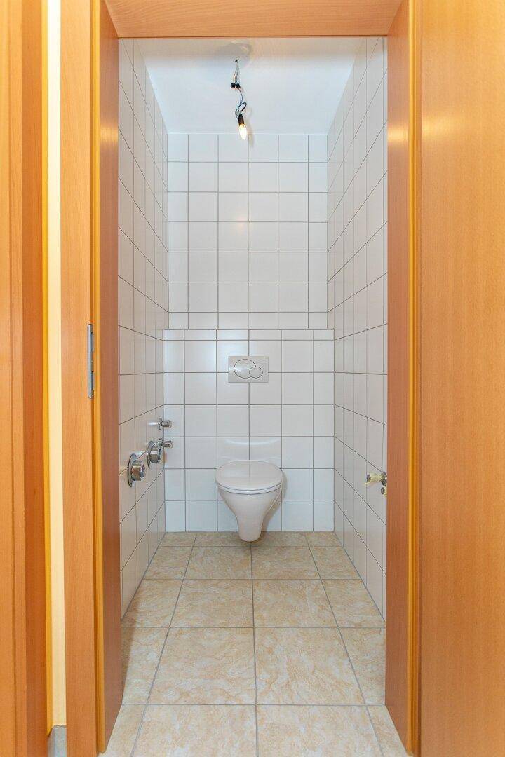 Separates WC mit Wand-WC und Fliesenboden in neutralen Farben.