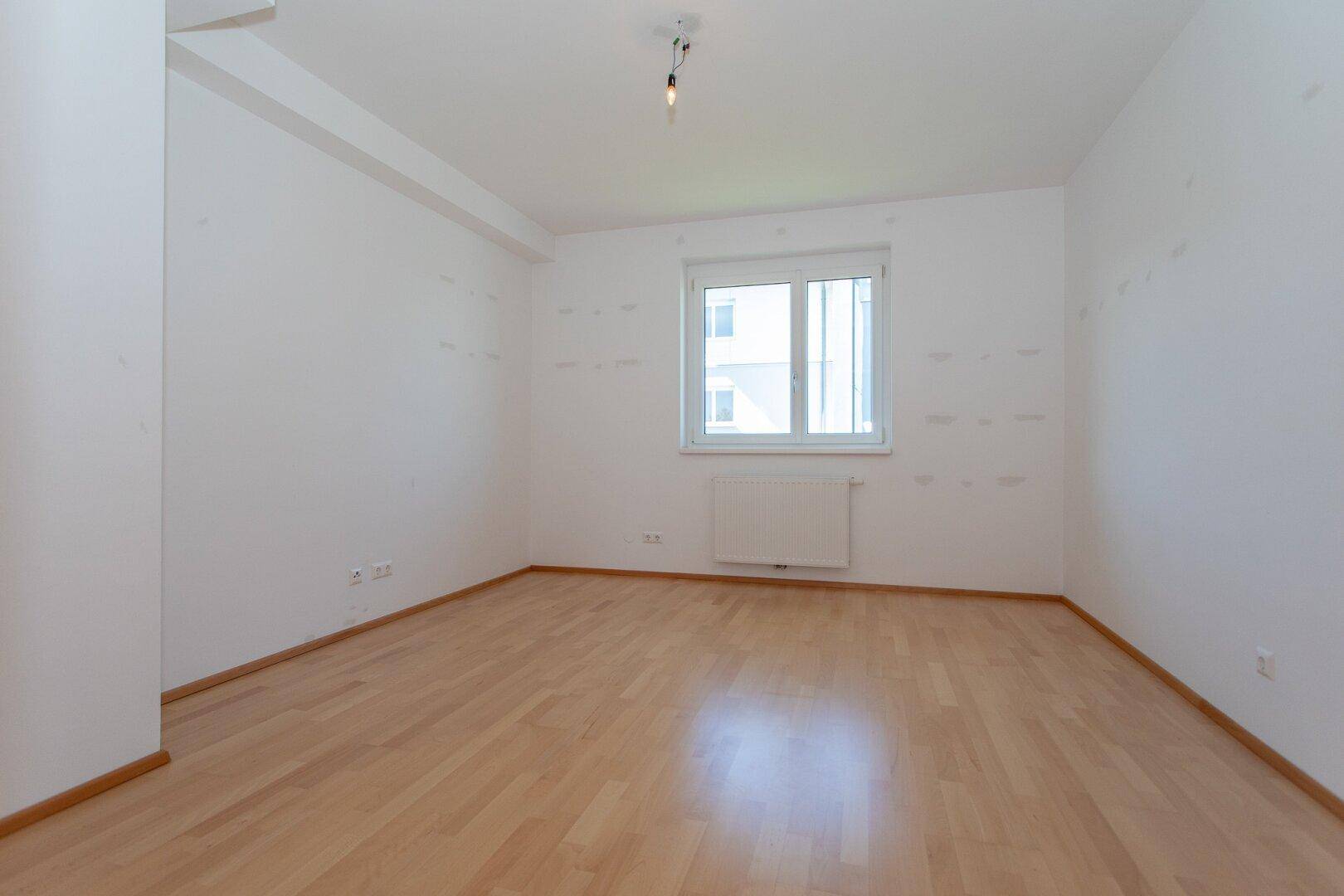 Geräumiges, helles Zimmer mit Parkettboden und einem großen Fenster.