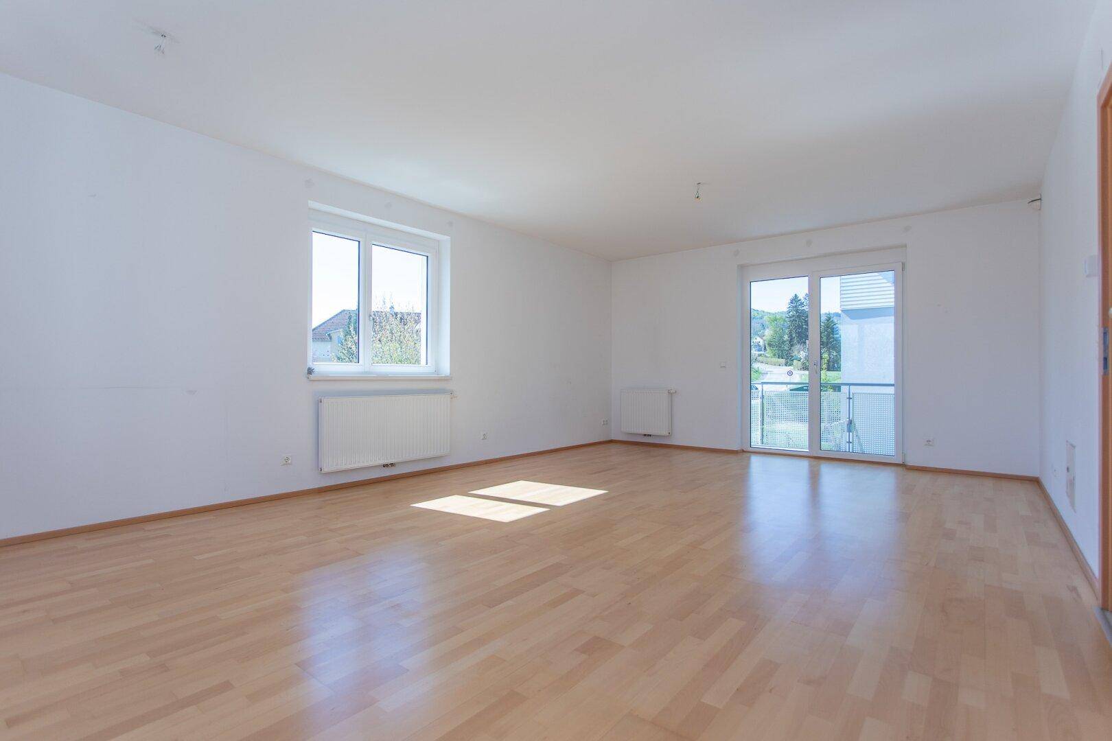 Lichtdurchfluteter Wohnbereich mit hellem Parkettboden und großzügigen Fenstern.
