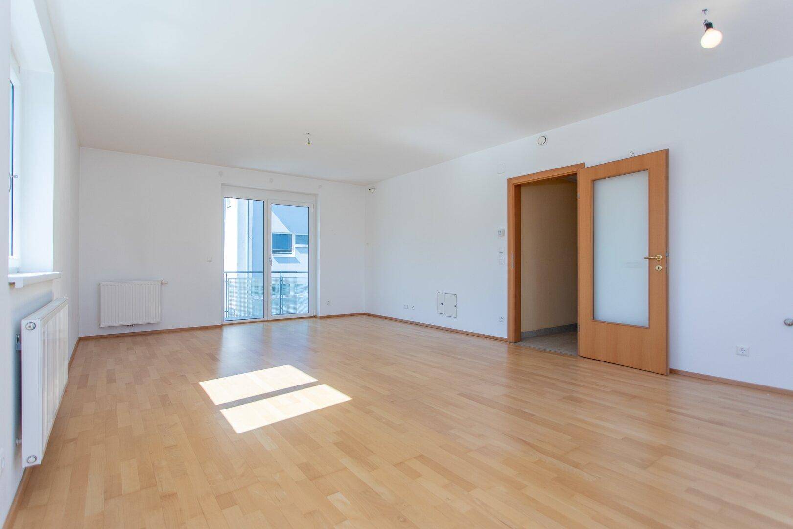 Geräumiges, helles Zimmer mit Parkettboden und Zugang zu einem weiteren Raum.