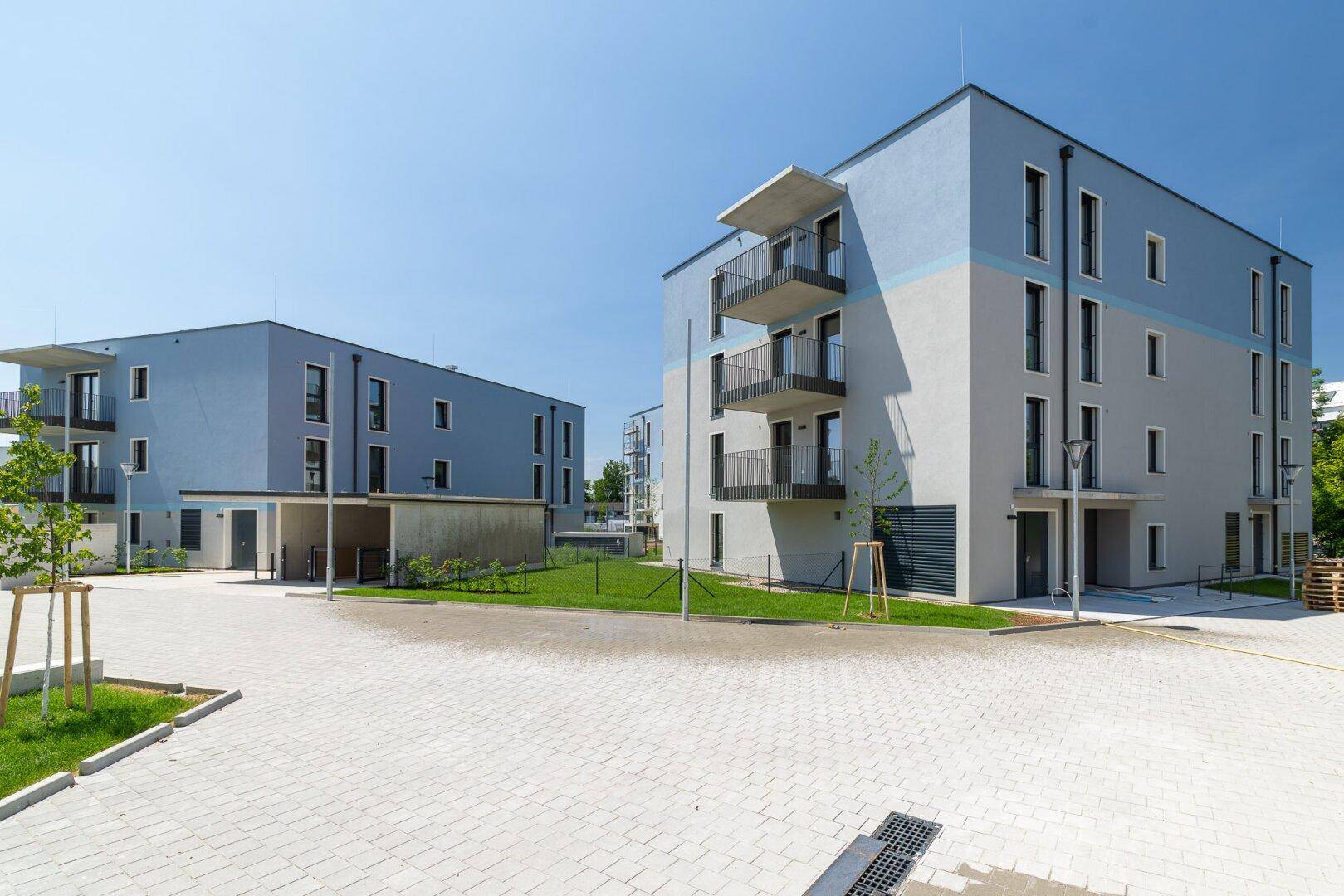 Mehrere moderne Wohngebäude mit hellblauen Fassaden, Balkonen und gepflasterten Wegen in einer Wohnanlage.