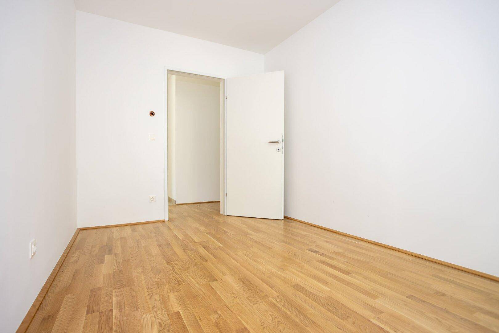 Unmöbliertes Zimmer mit Holzboden und weiß gestrichenen Wänden, bereit zur individuellen Einrichtung.