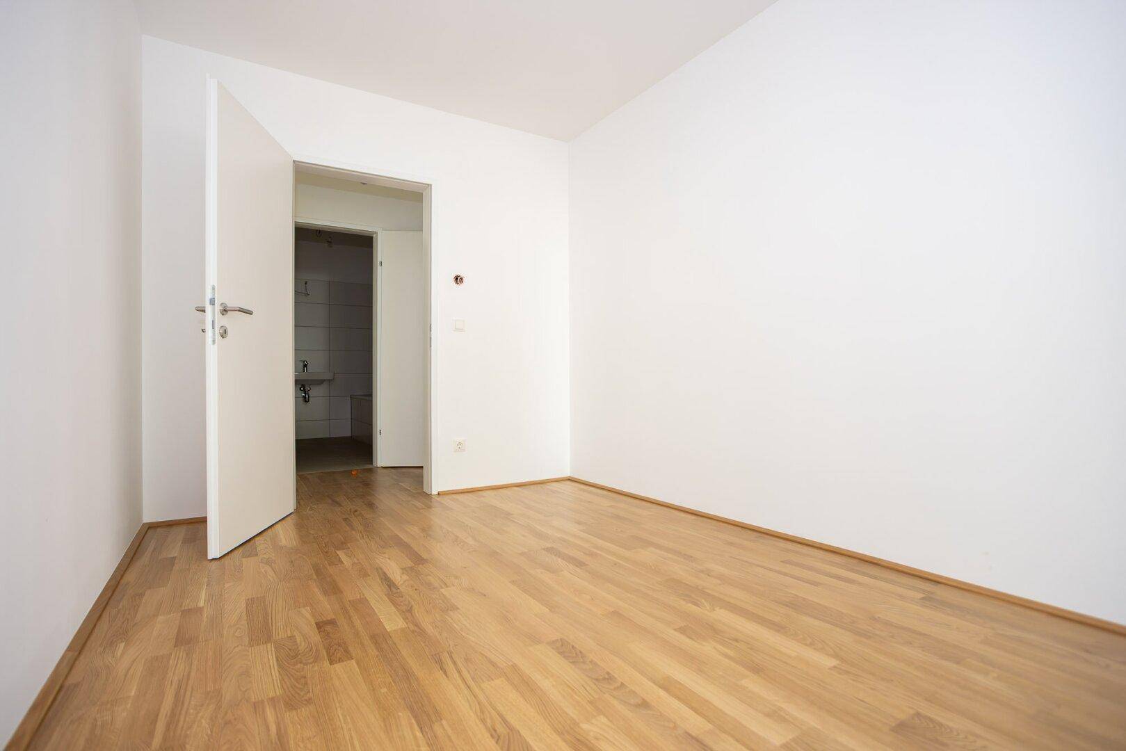 Geräumiges Zimmer mit Parkettboden und Zugang zu einem angrenzenden Badezimmer.