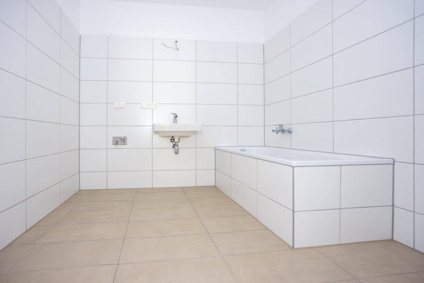 Geräumiges Badezimmer mit Badewanne, weißen Fliesen und neutralem Boden, bereit zur Fertigstellung.