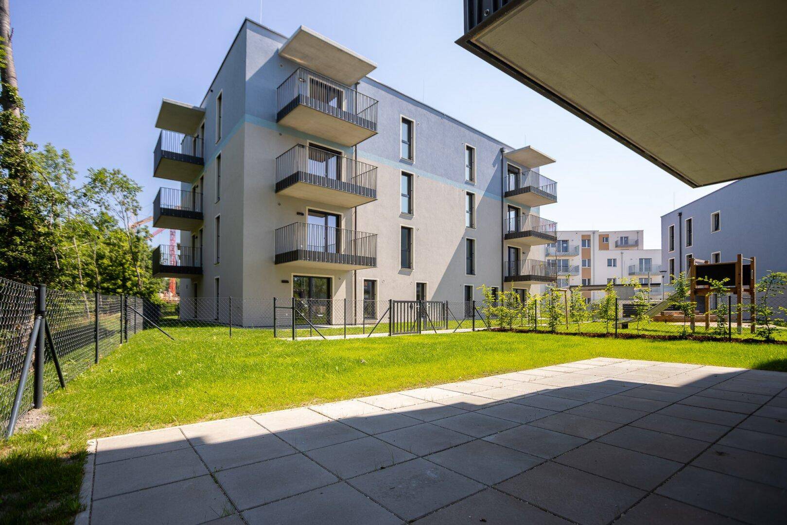 Moderne Wohnanlage mit großzügiger Terrasse und gepflegter Rasenfläche im Freien.