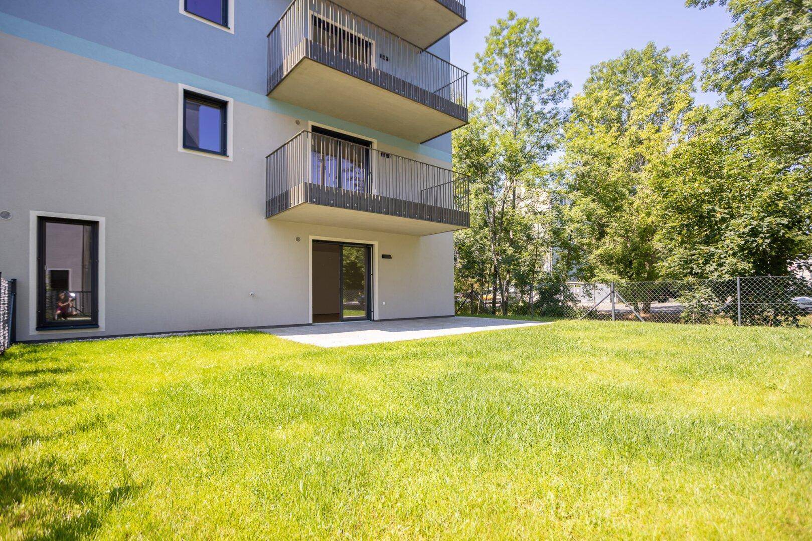 Sonniger Außenbereich mit Rasenfläche und Zugang zur Terrasse eines modernen Wohngebäudes.