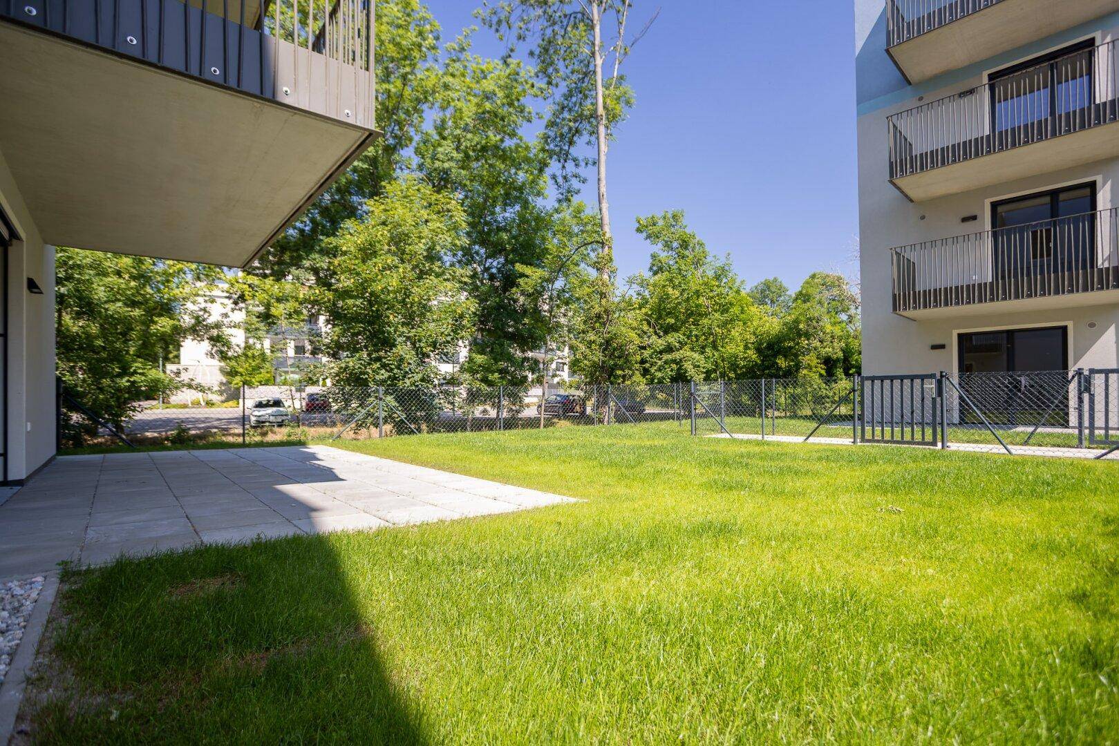 Sonniger Terrassenbereich mit Rasenfläche und Blick auf die umliegende Grünanlage.