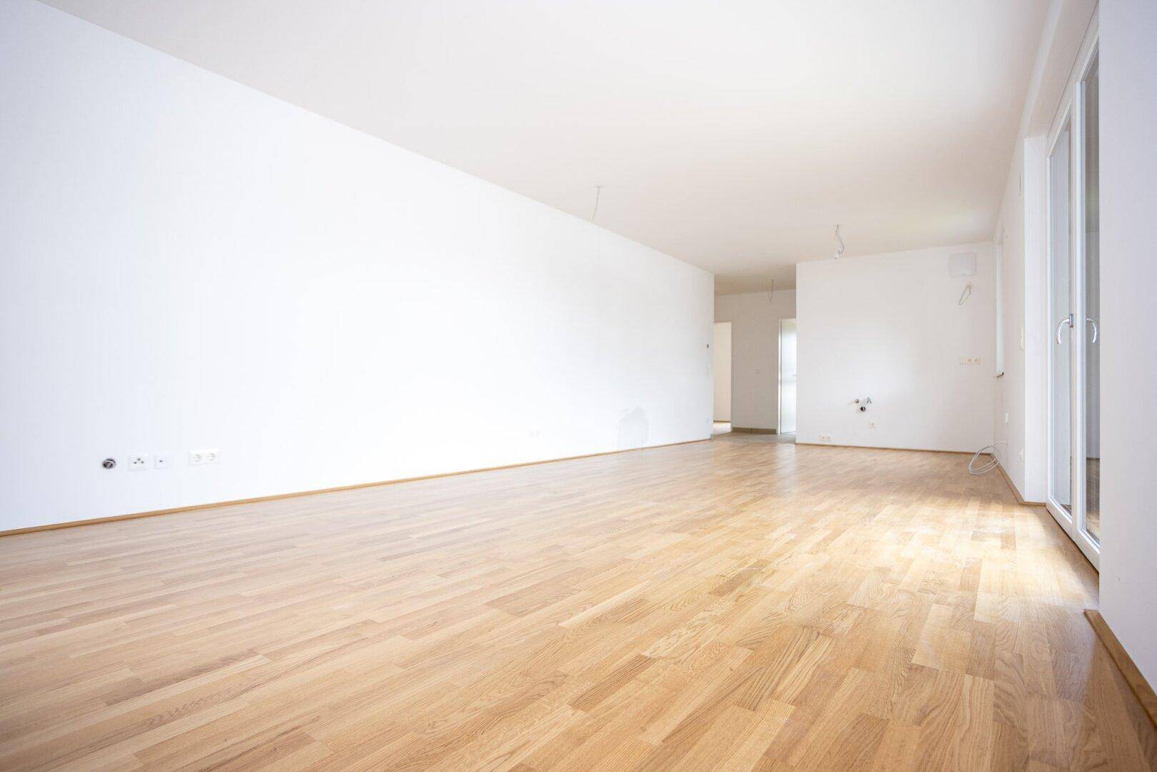 Lichtdurchfluteter Raum mit hellem Parkett und Zugang zu einem Balkon, ideal für offenes Wohnen.