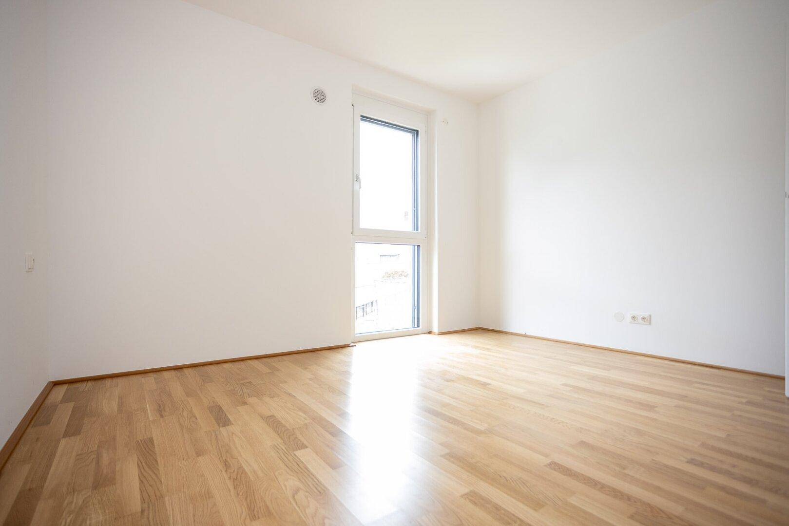Lichtdurchflutetes Zimmer mit Parkett und großem Fenster, ideal als Schlaf- oder Arbeitszimmer.