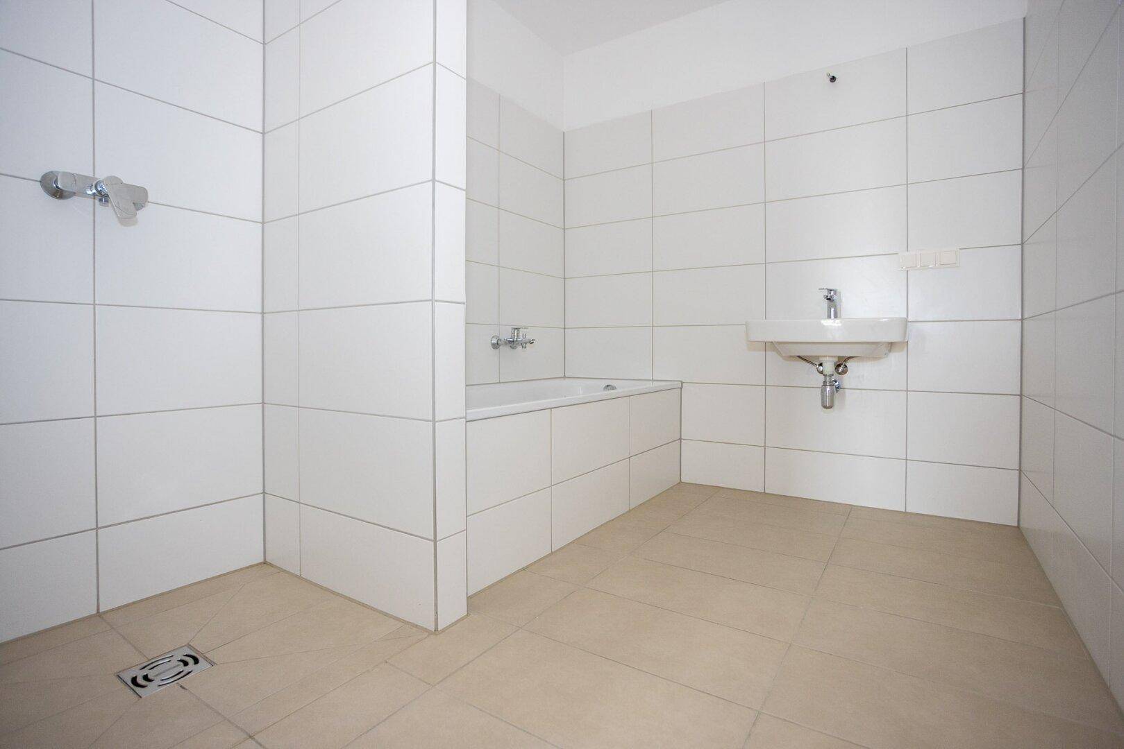Modernes Badezimmer mit weißen Wandfliesen, beigem Boden und integrierter Badewanne und Dusche.
