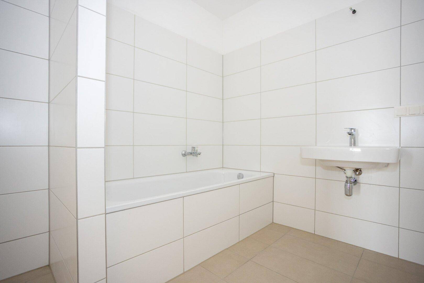 Helles Badezimmer mit weißen Fliesen, Badewanne und Waschbecken, in neuwertigem Zustand.