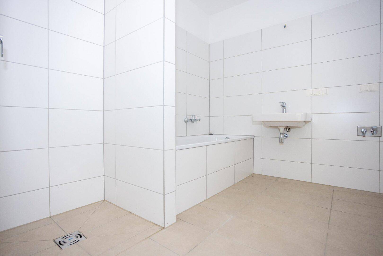 Modernes Badezimmer mit weißen Wandfliesen, beigem Boden und einer Badewanne mit Duschbereich.