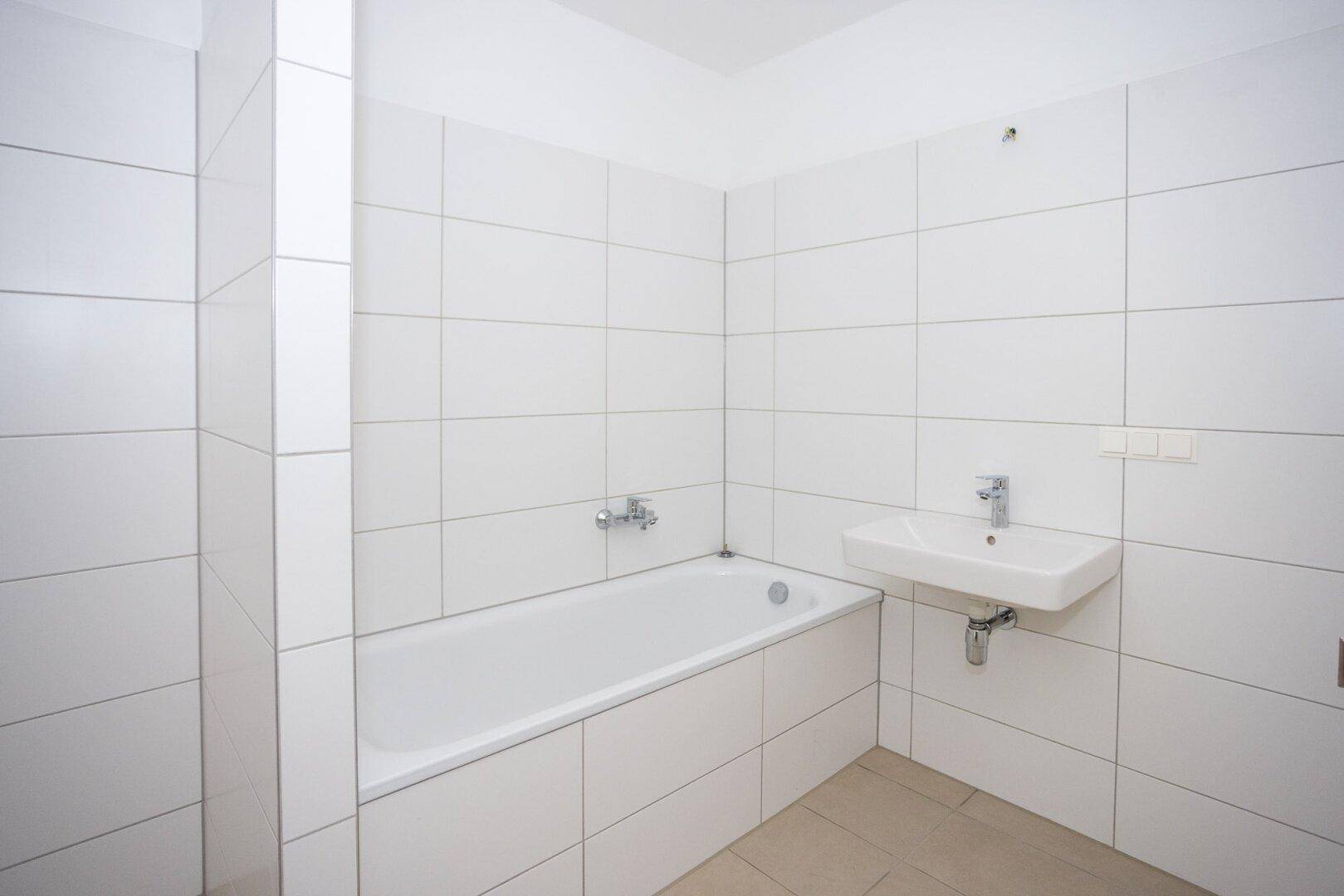Helles Badezimmer mit weißen Fliesen, Badewanne und einem modernen Waschbecken, bereit zur Nutzung.