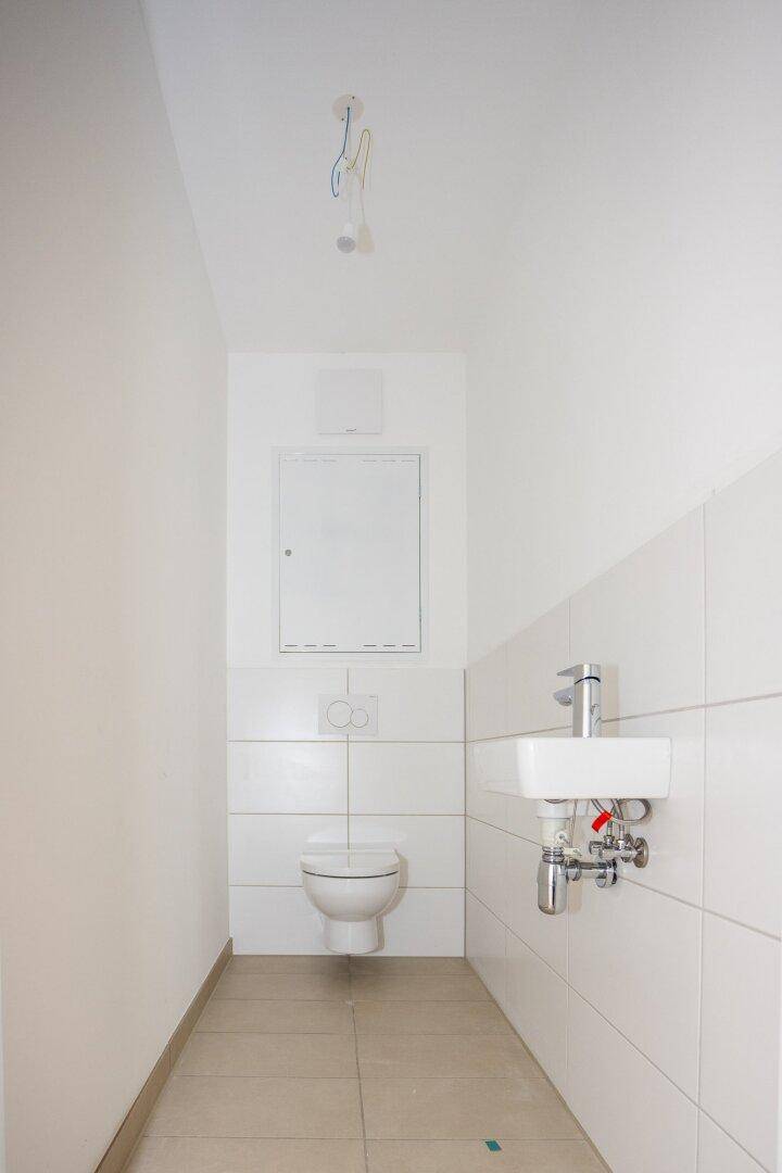 Kleines Gäste-WC mit wandhängender Toilette, kleinem Waschbecken und weißen Fliesen.