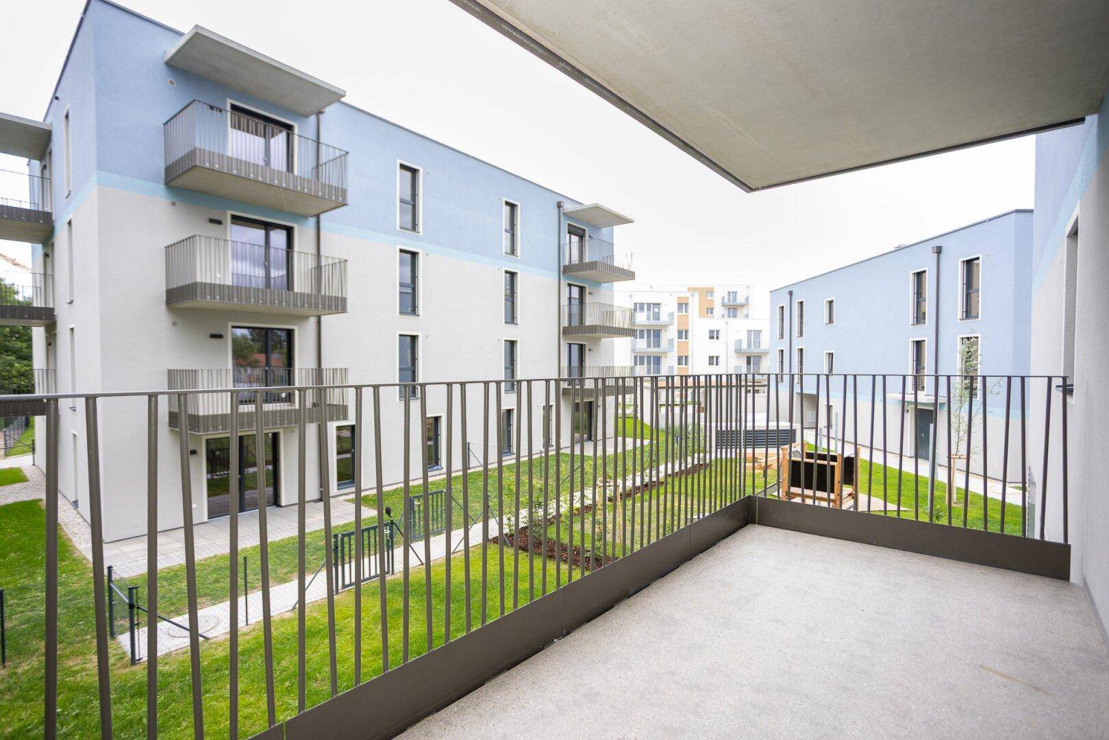 Balkon mit Blick auf den begrünten Innenhof und moderne Wohngebäude der Anlage.