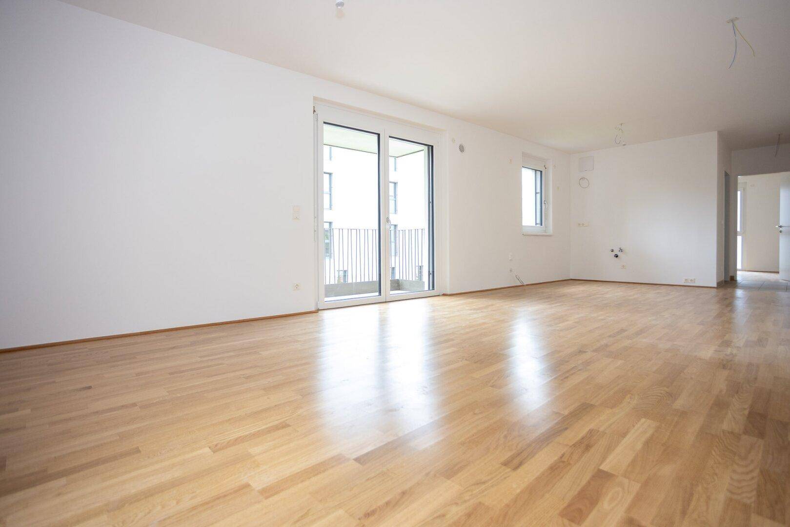 Geräumiges, helles Zimmer mit Holzboden und Schiebetür zum Balkon, bereit für die Einrichtung.