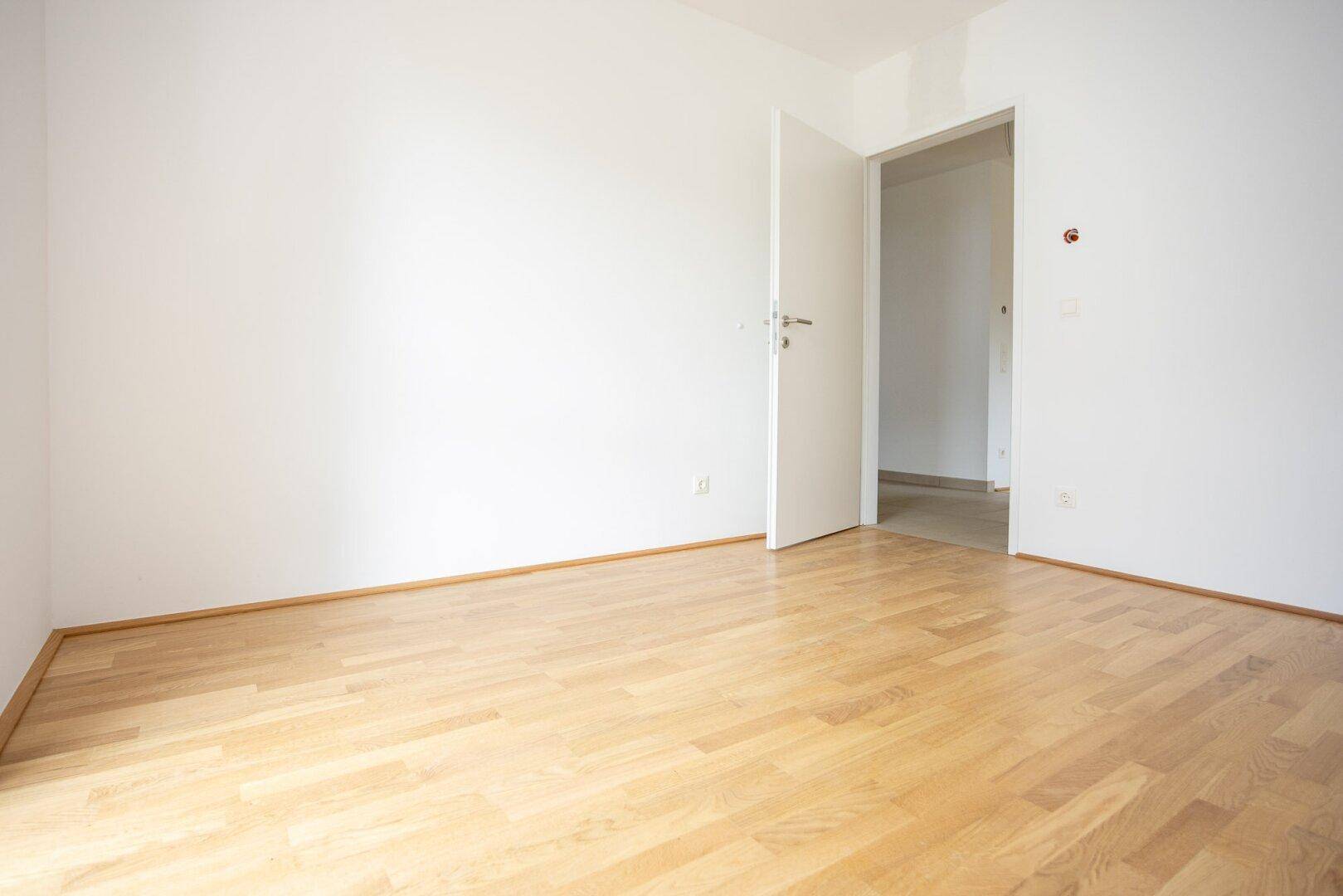 Helles Schlafzimmer mit Parkettboden und weiß gestrichenen Wänden, bereit zur individuellen Gestaltung.