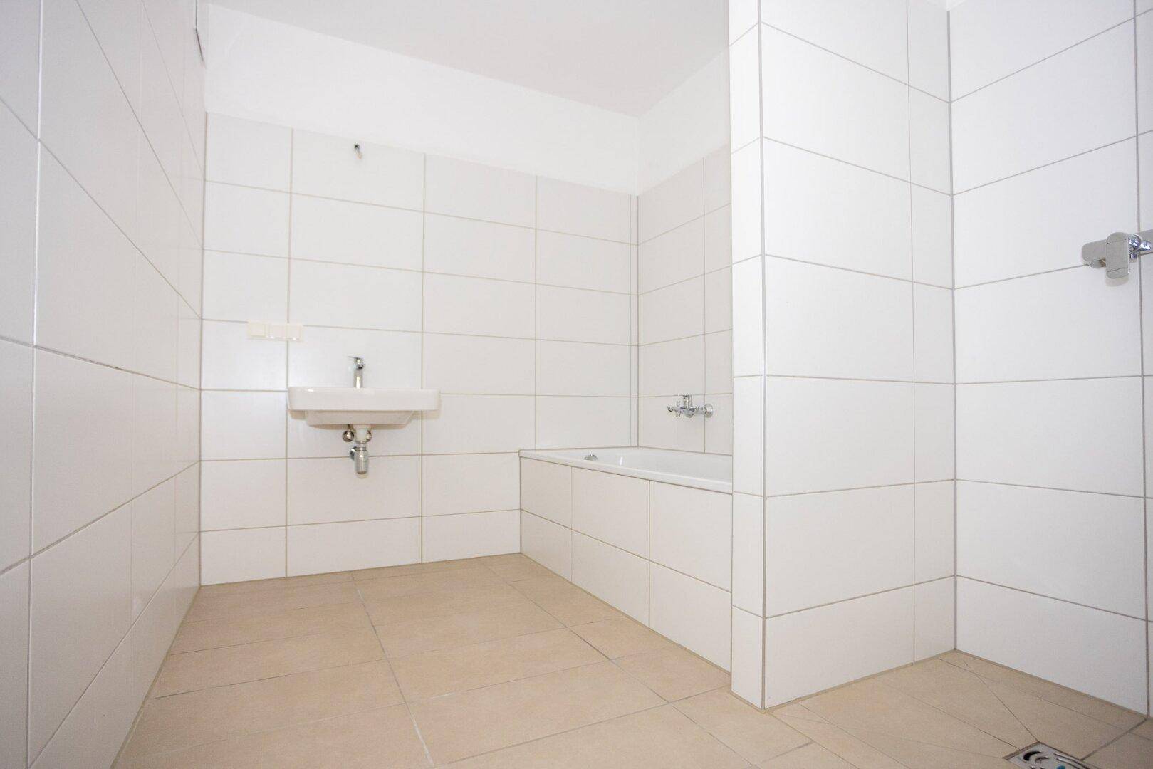 Modernes Badezimmer mit weißen Wandfliesen, beigen Bodenfliesen, Waschbecken und Badewanne.